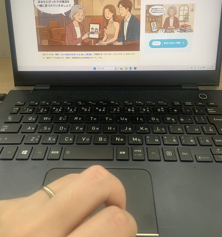 『真心マッチ』運営責任者「ぱんこす」（カタオカコウジ）の執筆風景。左手薬指に指輪をした既婚の管理人が、ノートパソコンで公式サイトを確認しながら記事を作成している手元の様子。（実写）