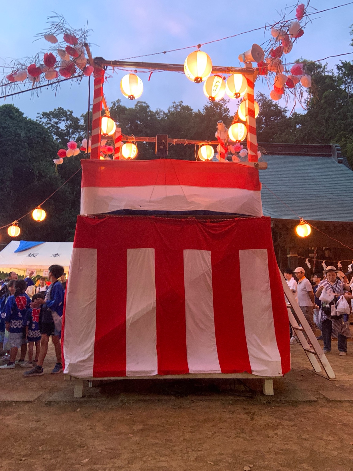 第六社の夏祭りで撮影したやぐら。提灯の明かりが灯る中、紅白の幕と子どもたちの法被姿がにぎやかさを演出している。